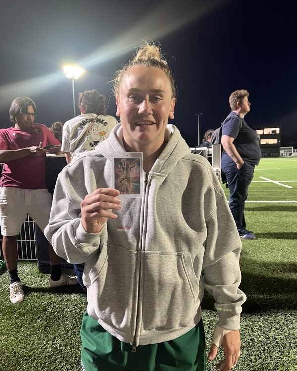Meg Jones smiling and holding her own signed Made By Stories trading card pitchside