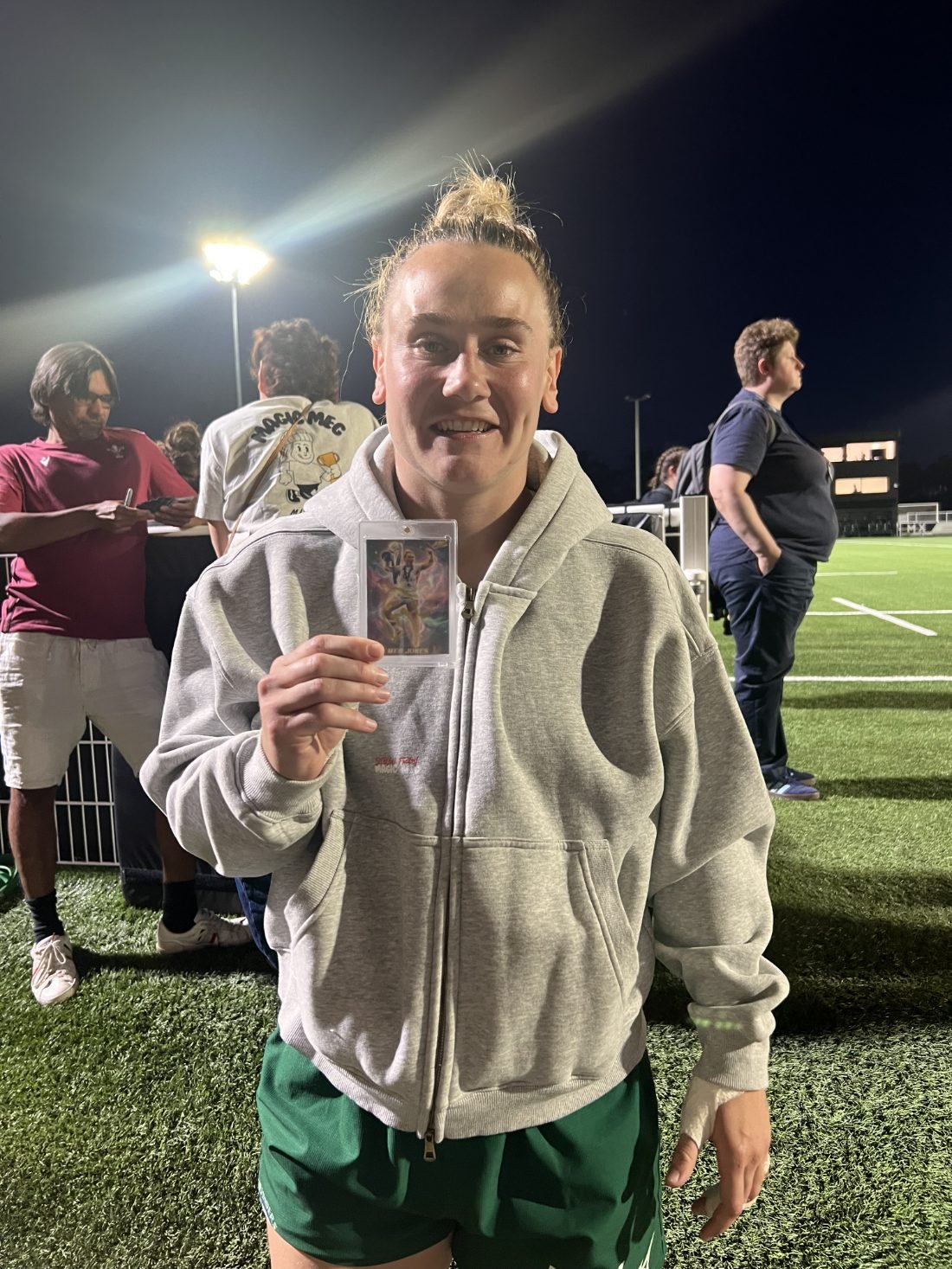 Meg Jones smiling and holding her own signed Made By Stories trading card pitchside